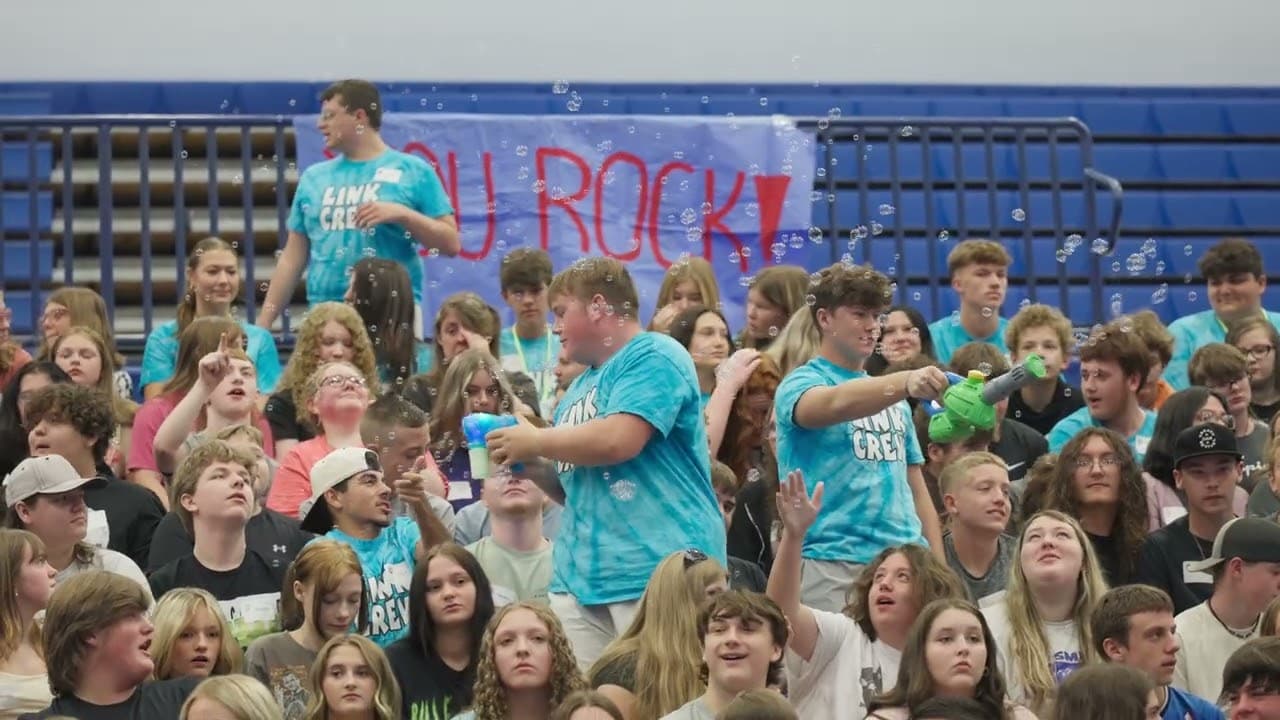 Students in matching Link Crew shirts cheering in a gym as bubbles float through the crowd