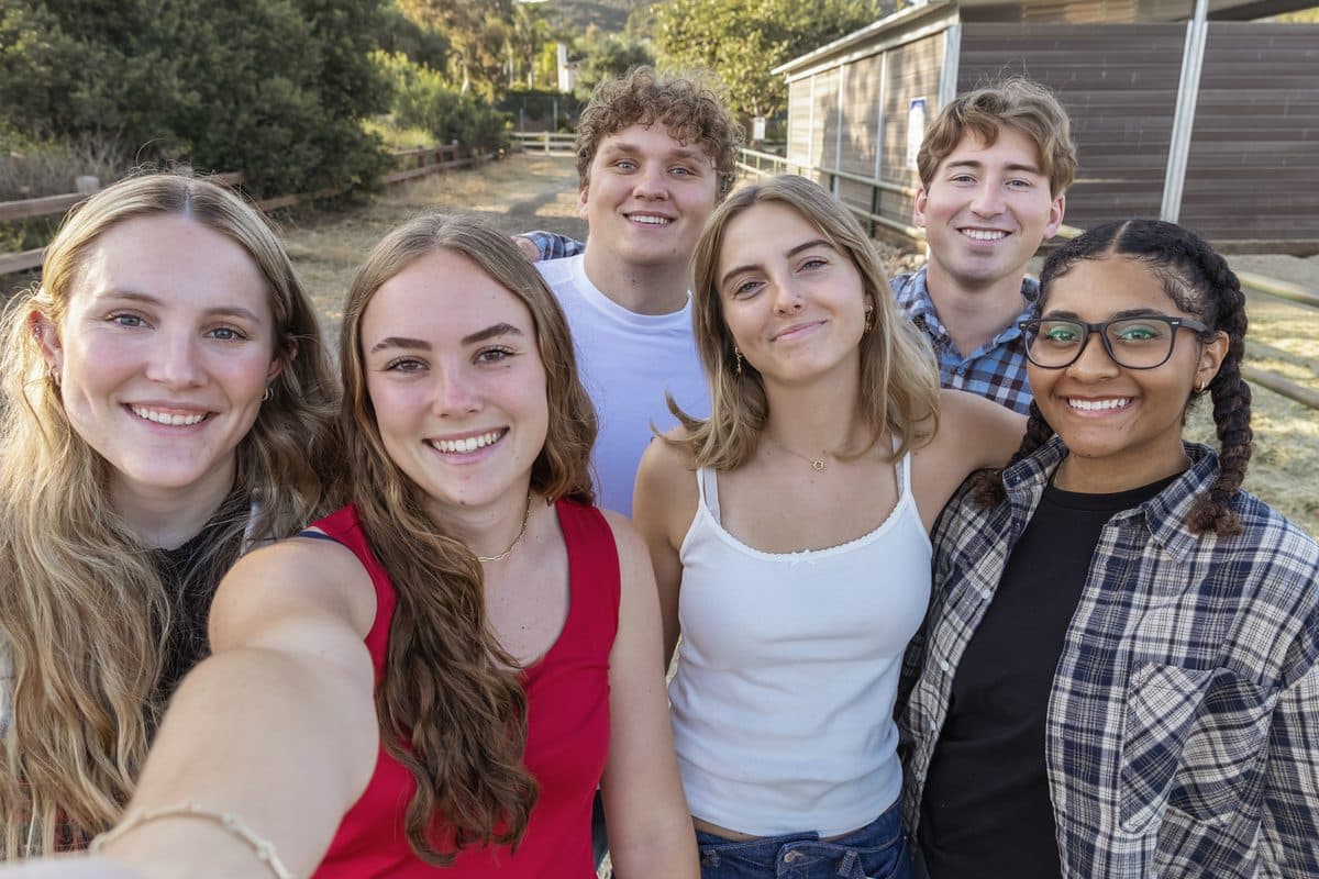 Six young people smiling for a group photo outside a farm building