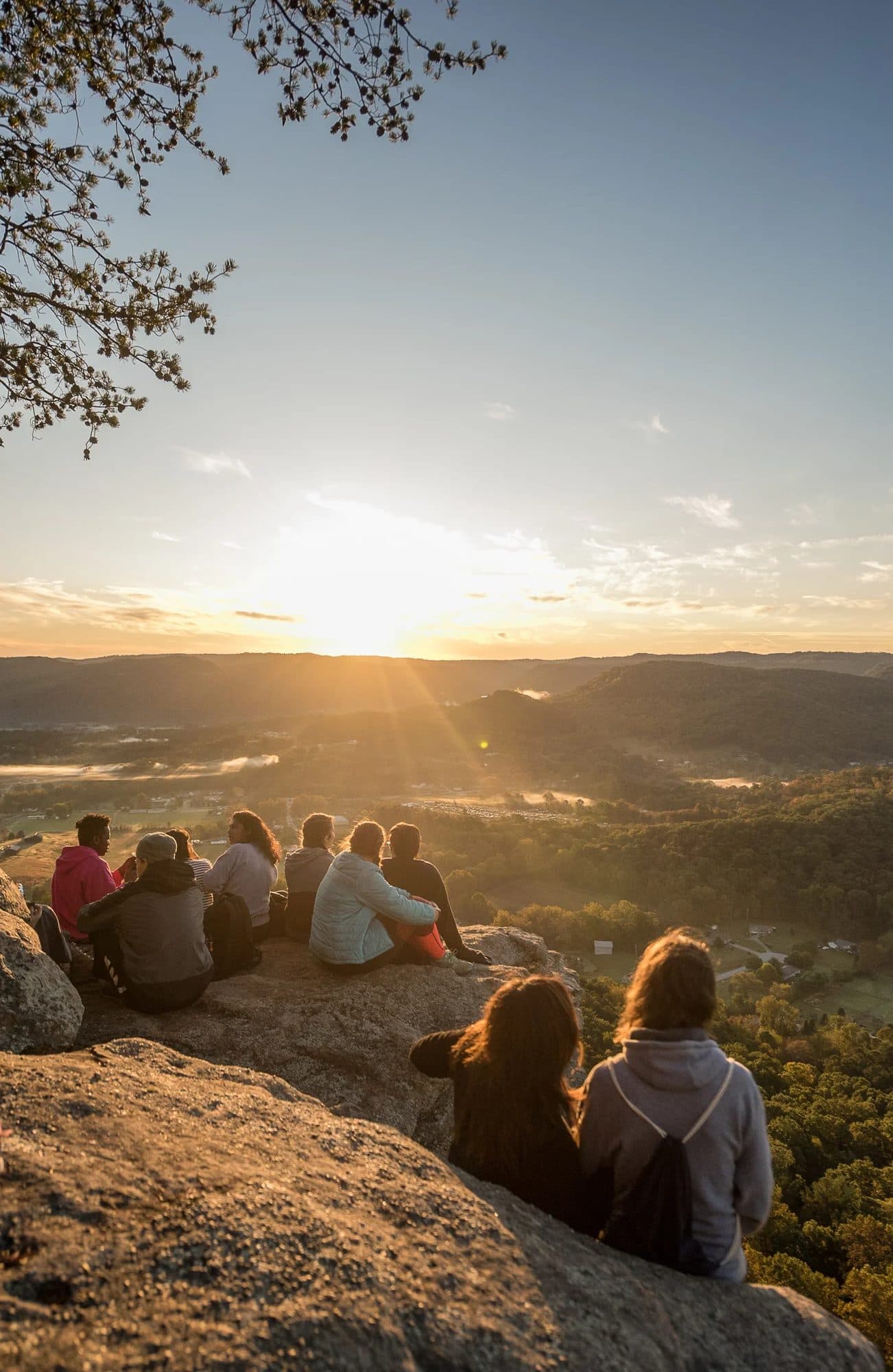 Young people sitting on a rock ledge watching the sun set over Appalachian hills