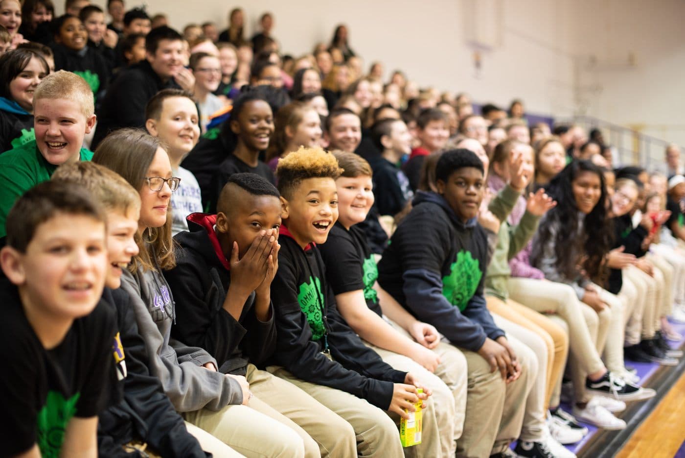 Students in matching shirts laughing together on gymnasium bleachers