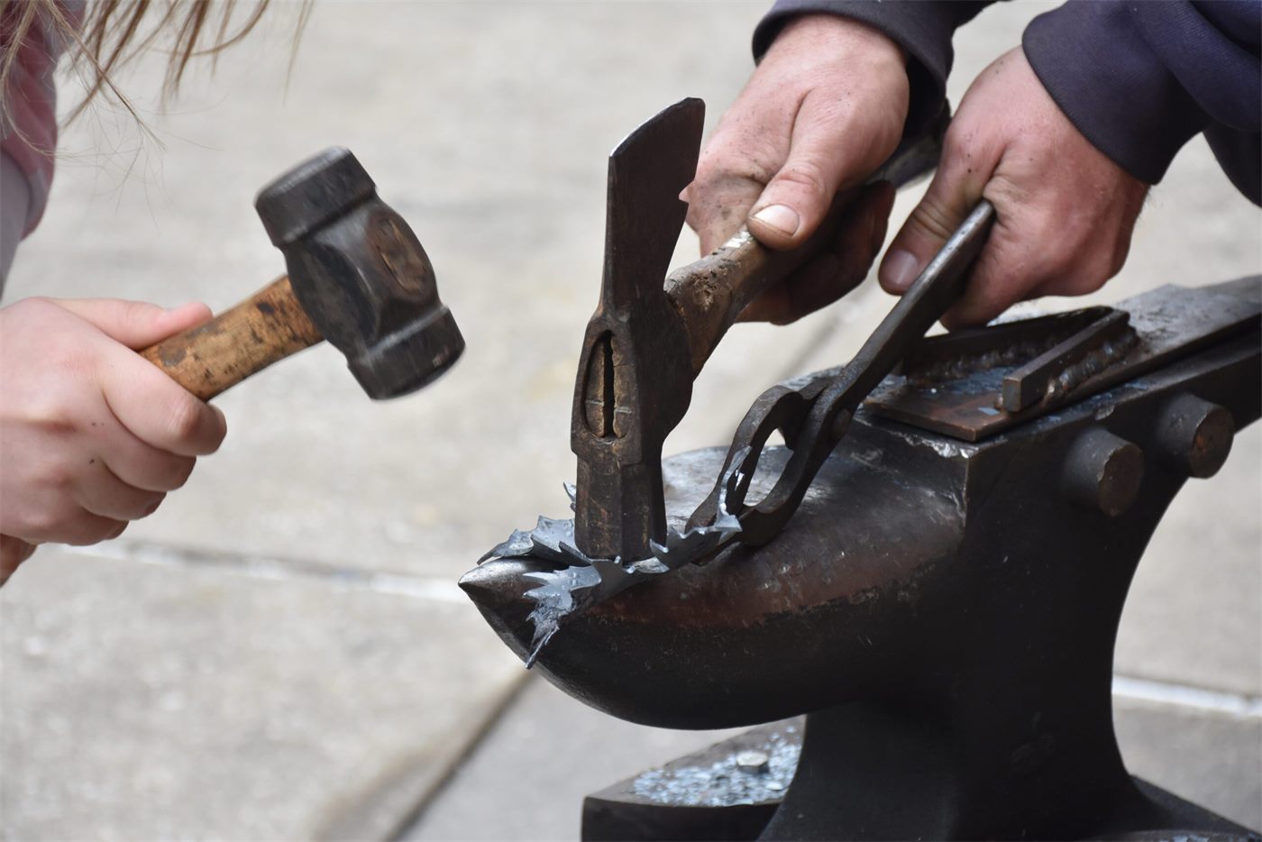 A hammer hitting a piece of steel shaped into a leaf on an anvil
